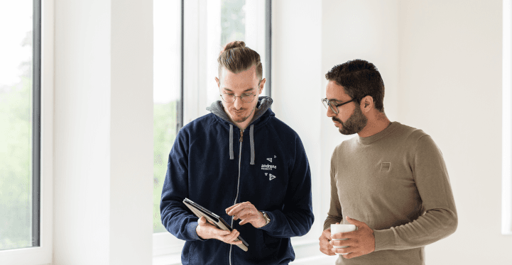 Zwei stehende Entwickler beraten sich, einer hält ein Tablet